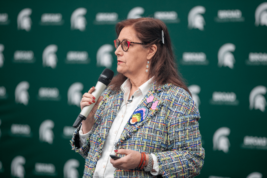 Woman speaking into a microphone in front of a Broad College of Business backdrop during a formal presentation.