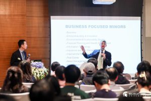 Max Olivero stands in front of a projection screen speaking to a group of seated students