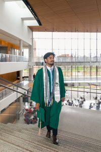 Student walking up stairs in a graduation gown holding a graduation cap