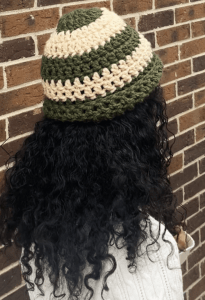 Person with long dark hair wearing a beanie, facing away from the camera in front of a brick wall
