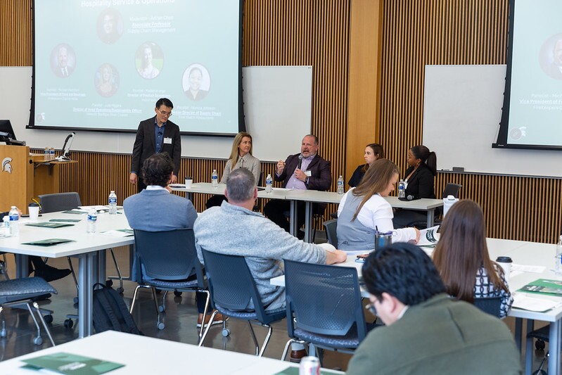 Panel speakers sitting at the front of the room speaking with symposium attendees.