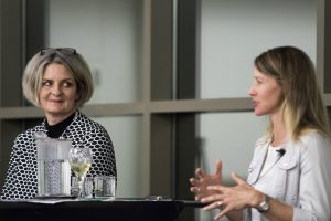 One woman panelist watches as another woman panelist speaks. 