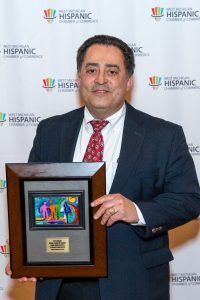 A man in a navy suit, white shirt and red tie holds his award