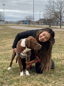 MBA student Erica Rochana smiles looking at her foster dog Chester, outside in a field.