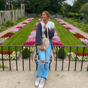 Broad student Gabby Rosely leaning on a fence in front of a lush flower garden.